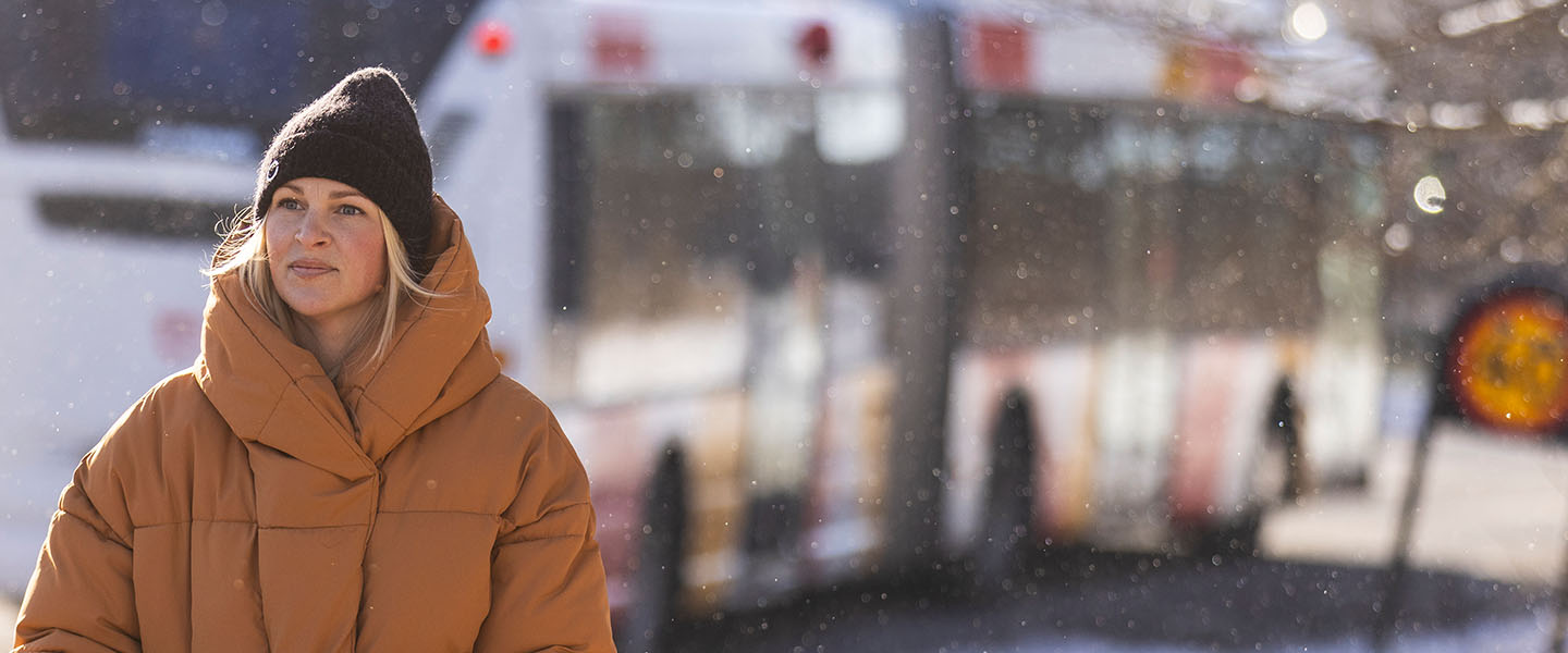 En kvinna med tjock mössa och jacka går från en buss.
