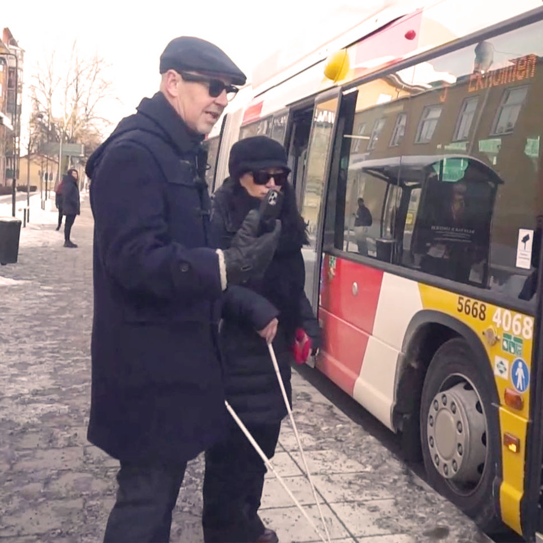 Två personer med vita käppar på väg att gå på en buss.