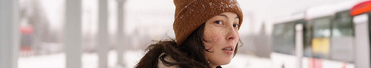 En tonåring med blå jacka går emot snö som blåser i ansiktet på henne.